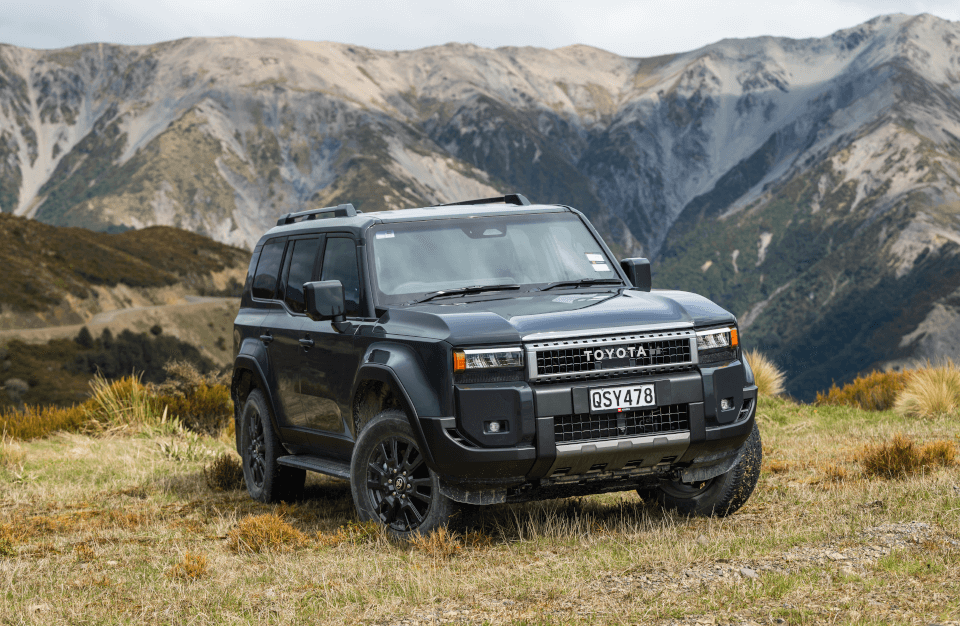 A Toyota Prado parked on grass with a mountain range in the background